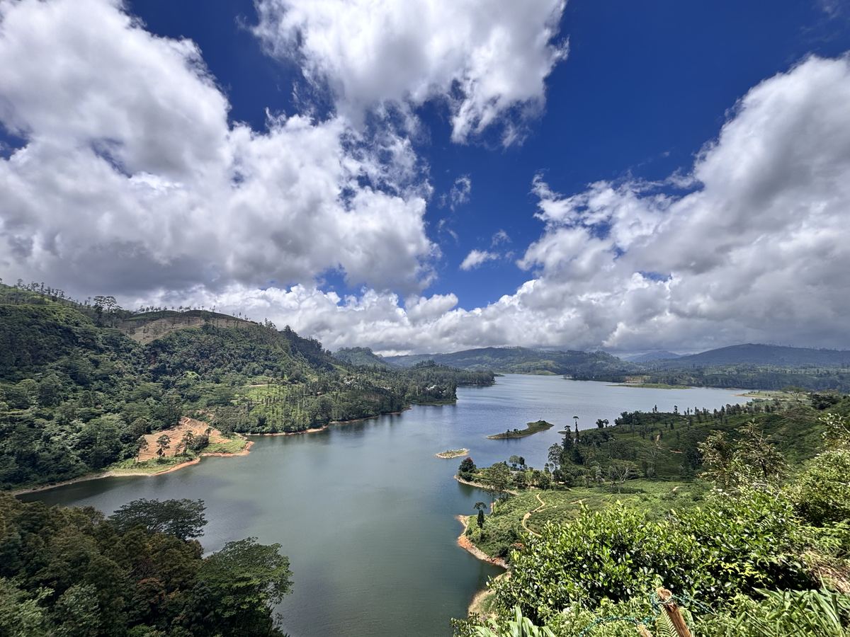 Stausee zwischen bewaldeten Hügeln, darüber ein Himmel voller Quellwolken