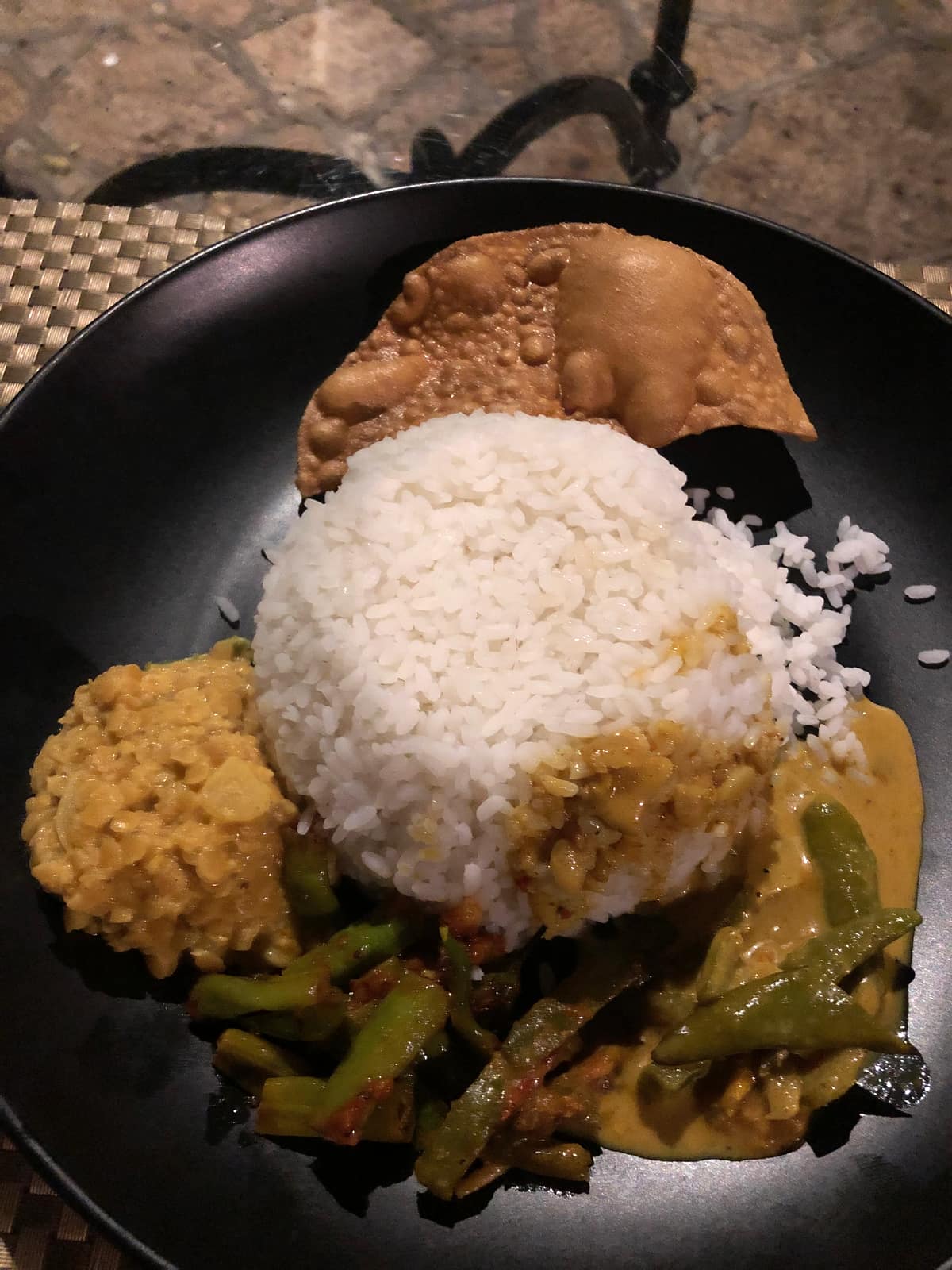 Rice and Curry am Abend: Reis, Dhal, Papadam und Gemüsecurry auf schwarzem Teller